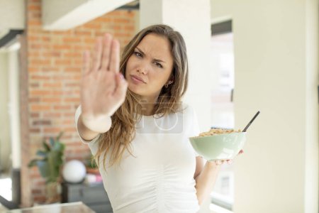 Foto de Bonita mujer mirando en serio mostrando la palma abierta haciendo gesto de parada. concepto de plato de desayuno - Imagen libre de derechos