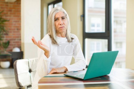 Photo for Senior pretty woman shrugging, feeling confused and uncertain with a laptop - Royalty Free Image