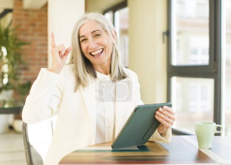 Téléchargez les photos : Senior jolie femme se sentant comme un génie heureux et excité après avoir réalisé une idée avec un écran tactile - en image libre de droit