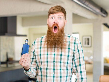 Photo for Red hair man feeling extremely shocked and surprised with a vaper - Royalty Free Image