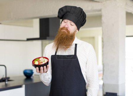 Foto de Hombre de pelo rojo sonriendo y mirando con una expresión segura feliz con un cuenco de ramen. concepto de chef - Imagen libre de derechos