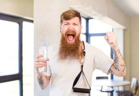 Foto de Hombre de pelo rojo que parece enojado, molesto y frustrado con una botella de agua. concepto de fitness - Imagen libre de derechos
