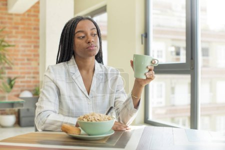 Téléchargez les photos : Afro femme noire souriante et regardant avec une expression heureuse et confiante. concept de petit déjeuner - en image libre de droit