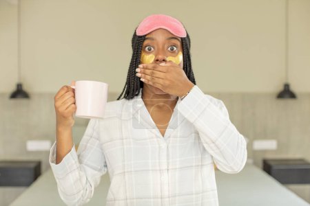 Photo for Black afro woman covering mouth with a hand and shocked or surprised expression. rest and nightwear concept - Royalty Free Image
