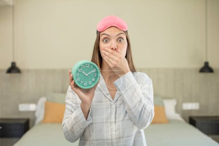 Photo for Young pretty woman covering mouth with a hand and shocked or surprised expression. alarm clock concept - Royalty Free Image