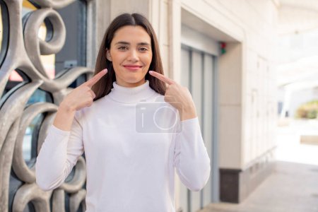 Téléchargez les photos : Pretty young adult woman smiling confidently pointing to own broad smile, positive, relaxed, satisfied attitude - en image libre de droit