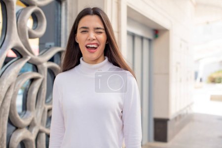 Téléchargez les photos : Pretty young adult woman looking happy and friendly, smiling and winking an eye at you with a positive attitude - en image libre de droit