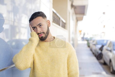 Photo for Young handsome man feeling bored, frustrated and sleepy after a tiresome, dull and tedious task, holding face with hand - Royalty Free Image