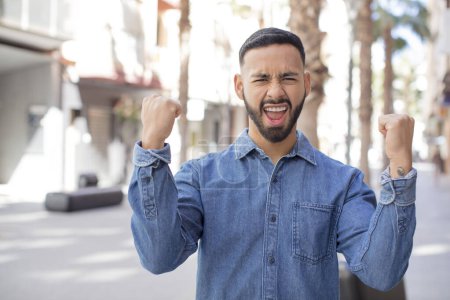 Photo for Young handsome man shouting aggressively with an angry expression or with fists clenched celebrating success - Royalty Free Image