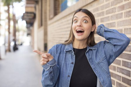 Téléchargez les photos : Jeune jolie femme riant, regardant heureux, positif et surpris, réalisant une grande idée pointant vers l'espace de copie latérale - en image libre de droit