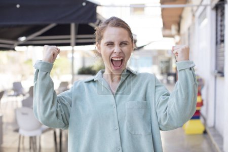 Photo for Pretty young woman shouting aggressively with an angry expression or with fists clenched celebrating success - Royalty Free Image