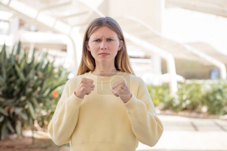 Foto de Mujer joven bonita mirando confiado, enojado, fuerte y agresivo, con puños listos para luchar en posición de boxeo - Imagen libre de derechos