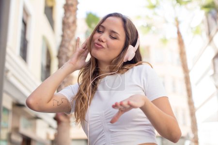 Téléchargez les photos : Hispanique jolie femme écouter de la musique avec écouteurs - en image libre de droit