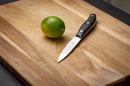 Green citrus fruit placed next to a knife on a cutting board