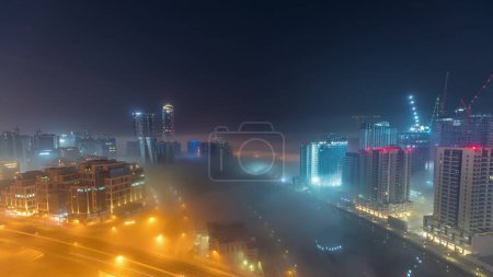 Foto de Los edificios están cubiertos de una gruesa capa de niebla en Business Bay durante toda la noche. Rascacielos iluminados alrededor del canal de agua vista aérea - Imagen libre de derechos