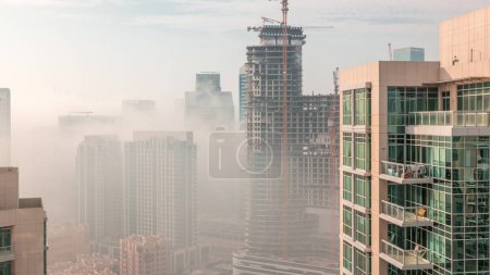 Photo for Dubai skyscrapers covered by morning fog in business bay district with construction site during sunrise timelapse. Aerial view from top of downtown in United Arab Emirates. - Royalty Free Image