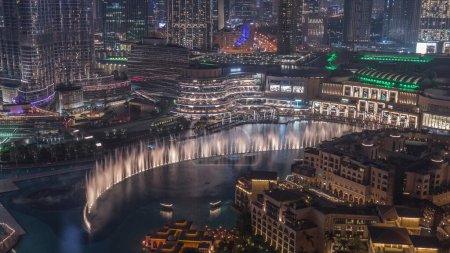 Photo for Dubai Fountain aerial night timelapse. Musical fountain, located in an artificial lake in downtown. Top view from above with evening illumination and old town houses - Royalty Free Image