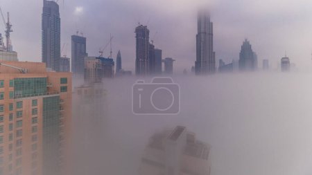 Foto de Vista aérea de la ciudad de Dubai temprano en la mañana durante el timelapse niebla. Salida del sol en el horizonte futurista de la ciudad con rascacielos y torres desde arriba. Sol reflejado desde la superficie de vidrio con rayos de luz - Imagen libre de derechos