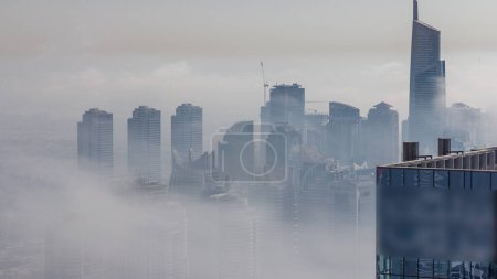 Photo for Fog covered skyscrapers in JLT district aerial timelapse. Top view from Dubai marina towers at evening time - Royalty Free Image