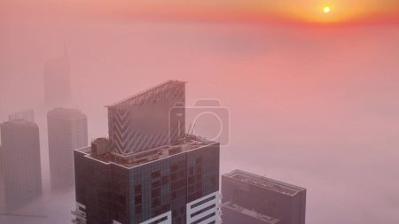 Téléchargez les photos : Lever du soleil sur un brouillard hivernal rare tôt le matin au-dessus de la ligne d'horizon de Dubai Marina et des gratte-ciel éclairés par la lumière du soleil orage intemporel aérien. Vue de dessus depuis les nuages. Dubai, Émirats arabes unis - en image libre de droit