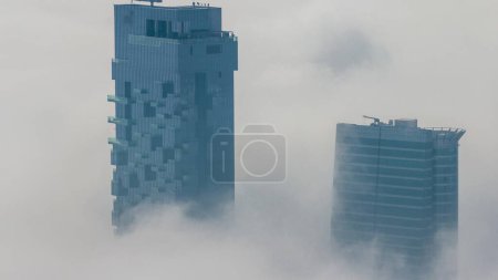 Téléchargez les photos : Le brouillard couvrait les gratte-ciel et les tours de marina de la JLT près de Sheikh Zayed Road après le lever du soleil. Immeuble résidentiel matin brumeux - en image libre de droit