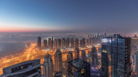 Photo for Panorama of Dubai Marina with JLT skyscrapers and golf course night to day transition timelapse, Dubai, United Arab Emirates. Aerial view from above towers foggy morning. City skyline with rooftops - Royalty Free Image