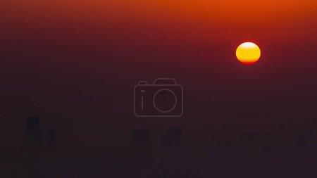 Foto de Salida del sol vista de cerca sobre el horizonte de Dubai por la mañana, vista aérea desde Dubai Marina timelapse. Gran sol en el cielo naranja se eleva sobre la niebla alrededor de los rascacielos. Emiratos Árabes Unidos - Imagen libre de derechos