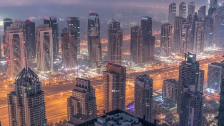 Photo for JLT skyscrapers and marina towers near Sheikh Zayed Road aerial night to day transition timelapse. Illuminated residential buildings and skyline with villas. Foggy morning before sunrise - Royalty Free Image