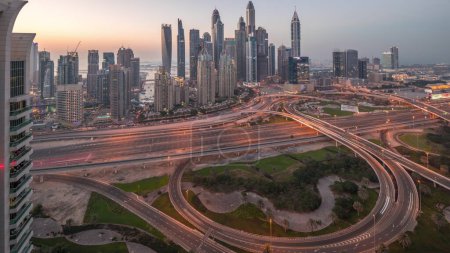 Téléchargez les photos : Panorama de Dubai Marina carrefour autoroutier spaghetti jonction jour-nuit passage timelapse. Les gratte-ciel les plus hauts éclairés sur un fond. Vue aérienne du quartier JLT après le coucher du soleil - en image libre de droit