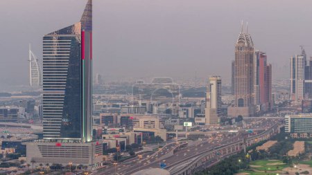 Foto de Vista aérea de Sheikh Zayed Road en Dubai Internet City área día a noche timelapse transición. Rascacielos y tráfico en una carretera con estación de metro después del atardecer - Imagen libre de derechos