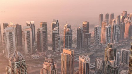 Photo for JLT skyscrapers and marina towers near Sheikh Zayed Road aerial timelapse during sunrise. Residential buildings and skyline with villas. Foggy morning during sunrise with warm orange light - Royalty Free Image