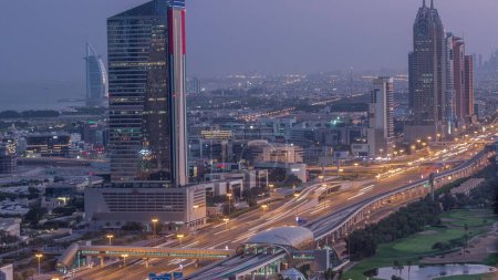 Téléchargez les photos : Vue aérienne de Sheikh Zayed Road dans la zone de Dubai Internet City avec des tours éclairées la nuit au jour passage timelapse. gratte-ciel et circulation sur une autoroute avec station de métro - en image libre de droit