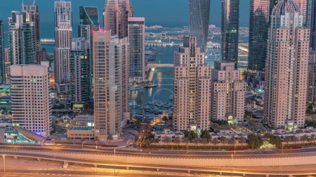Téléchargez les photos : Les gratte-ciel de Dubai Marina avec les bâtiments résidentiels les plus hauts éclairés nuit à la transition quotidienne timelapse. Vue aérienne du quartier JLT avant le lever du soleil. Yachts flottant sur l'eau - en image libre de droit