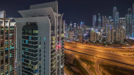 Téléchargez les photos : Panorama du port de plaisance de Dubaï montrant l'intersection de l'autoroute spaghetti jonction timelapse de nuit. Les gratte-ciel les plus hauts éclairés sur un fond. Vue aérienne du quartier JLT. - en image libre de droit