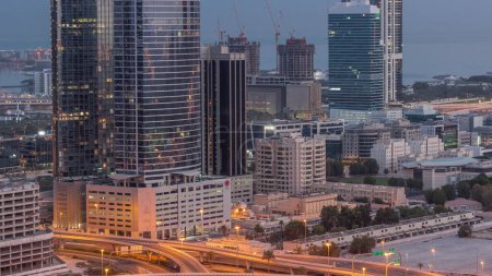Foto de Edificios de oficinas en Dubai Internet City y Media City distrito aéreo noche a día timelapse transición. Tráfico en cruce y rascacielos con amanecer y sol reflejado desde vidrio - Imagen libre de derechos