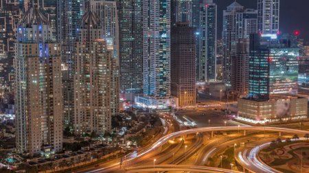 Photo for Aerial view on a big highway intersection night timelapse in Dubai Marina with skyscrapers around, UAE. Cars traffic view from JLT district. Illuminated towers with light in windows - Royalty Free Image