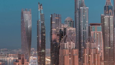 Téléchargez les photos : Les gratte-ciel de Dubai Marina avec les bâtiments résidentiels les plus hauts éclairés nuit à la transition quotidienne timelapse. Vue aérienne du quartier JLT. Soleil réfléchi par le verre au lever du soleil - en image libre de droit