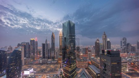 Foto de Panorama de rascacielos futuristas después del atardecer en el centro de negocios del distrito financiero en Dubai en el camino Sheikh Zayed día a noche timelapse transición. Vista aérea desde arriba con cielo nublado - Imagen libre de derechos