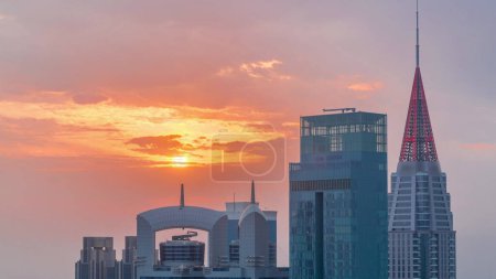 Foto de Puesta de sol sobre el centro financiero de la ciudad de Dubai con rascacielos de lujo timelapse, Dubai, Emiratos Árabes Unidos. Vista aérea con cielo anaranjado y tejados de torres con agujas - Imagen libre de derechos