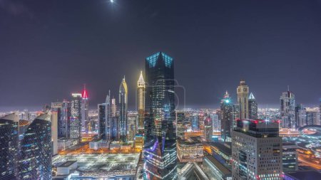Photo for Panorama of futuristic skyscrapers in financial district business center in Dubai on Sheikh Zayed road during all night timelapse. Aerial view from above with illuminated towers and moon - Royalty Free Image