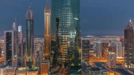Foto de Centro financiero de la ciudad de Dubai con rascacielos de lujo iluminados noche a día timelapse transición, Dubai, Emiratos Árabes Unidos. Vista aérea con luz en ventanas y torres de oficinas - Imagen libre de derechos