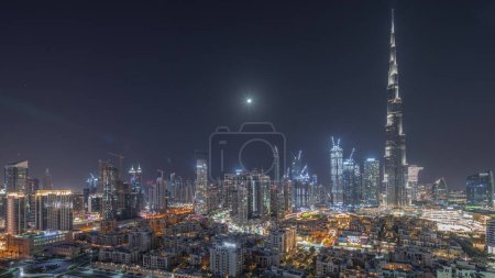 Foto de Dubai Downtown durante toda la noche con luna y luces apagando timelapse con rascacielos más altos y otras torres iluminadas vista panorámica desde la cima en Dubai, Emiratos Árabes Unidos. - Imagen libre de derechos