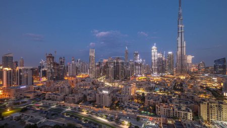Téléchargez les photos : Dubaï Temps de transition du centre-ville de nuit au jour avec des reflets sur le plus haut gratte-ciel et d'autres tours vue du haut pendant le lever du soleil, Émirats arabes unis. Maisons traditionnelles de la vieille ville et nuages roses - en image libre de droit