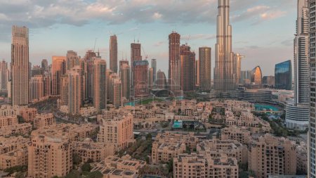 Téléchargez les photos : Dubaï Timelapse du matin au centre-ville avec le soleil reflété par le plus haut gratte-ciel et d'autres tours vue du haut pendant le lever du soleil, Émirats arabes unis. Maisons traditionnelles de la vieille ville et nuages roses - en image libre de droit