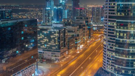 Téléchargez les photos : Les immeubles de bureaux de la baie d'affaires de Dubaï intemporel nuit aérienne avec la circulation de la rue. Vue sur le toit de certains gratte-ciel et de nouvelles tours en construction - en image libre de droit