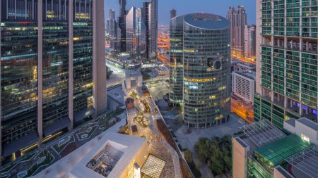 Photo for Dubai international financial center skyscrapers aerial night to day transition timelapse. Illuminated towers and walking area on a gate avenue panormic view from above before sunrise - Royalty Free Image