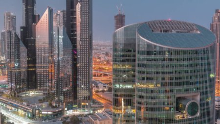 Téléchargez les photos : Centre financier international de Dubaï gratte-ciel aérien nuit au jour passage timelapse. Vue des tours éclairées d'en haut avant le lever du soleil. Trafic au carrefour et sur le chantier - en image libre de droit