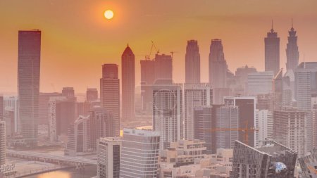 Téléchargez les photos : Skyline avec l'architecture moderne des tours de la baie d'affaires de Dubaï au coucher du soleil timelapse. Vue aérienne avec canal et chantier - en image libre de droit