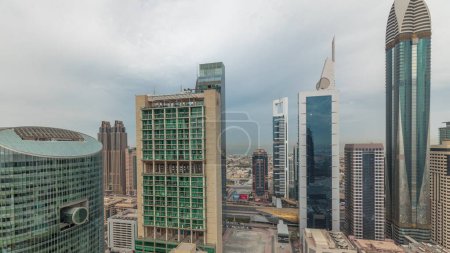 Foto de Panorama que muestra los rascacielos del centro financiero internacional de Dubái con paseo marítimo en un timelapse aéreo de la avenida de la puerta. Muchas torres de oficinas y el tráfico en una carretera. Cielo nublado - Imagen libre de derechos