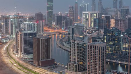 Photo for Skyline with modern architecture of Dubai business bay illuminated towers night to day transition timelapse. Aerial view with canal and construction site before sunrise - Royalty Free Image